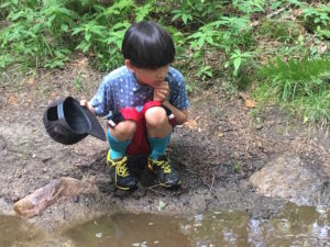 8 year old boy squats by a puddle, looking for frogs